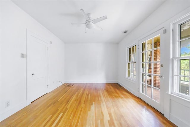 spare room featuring light wood finished floors, baseboards, visible vents, and a ceiling fan