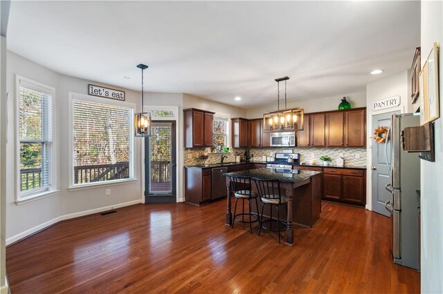 kitchen featuring a center island, dark wood-type flooring, stainless steel appliances, a kitchen breakfast bar, and pendant lighting