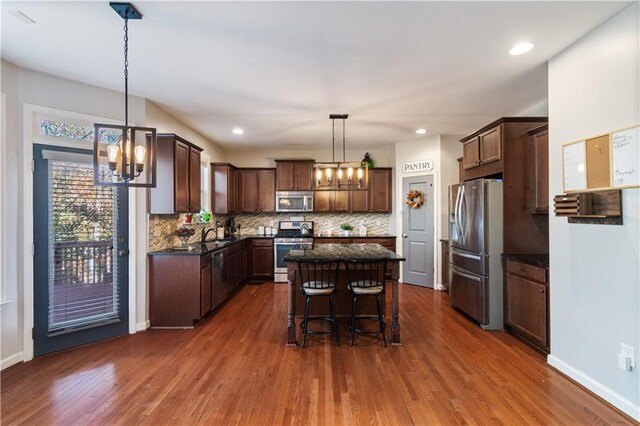 kitchen with a center island, dark wood-type flooring, hanging light fixtures, a kitchen bar, and stainless steel appliances