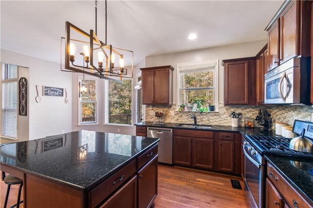 kitchen with a center island, an inviting chandelier, dark hardwood / wood-style floors, dark stone counters, and appliances with stainless steel finishes