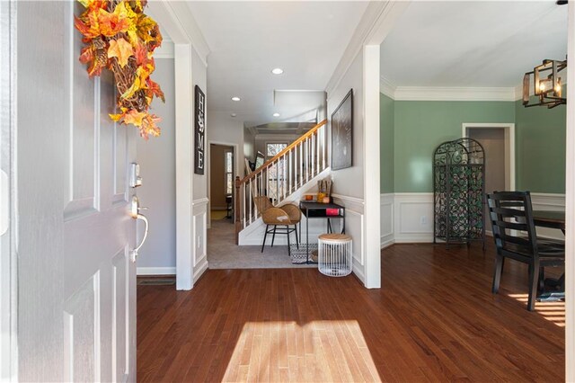 foyer entrance featuring crown molding, dark wood-type flooring, and an inviting chandelier