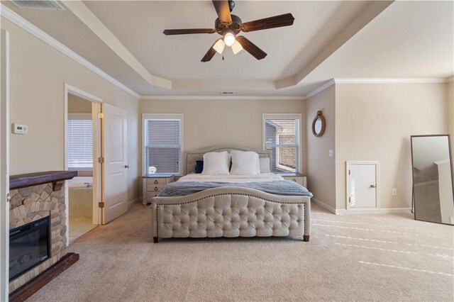 carpeted bedroom featuring a raised ceiling, ceiling fan, a stone fireplace, and ornamental molding