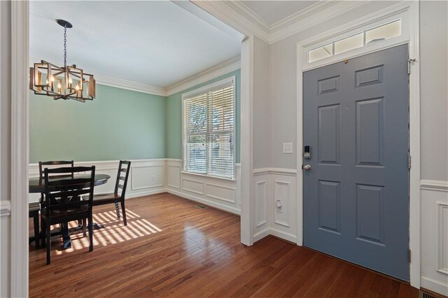 foyer entrance with hardwood / wood-style flooring, ornamental molding, and an inviting chandelier