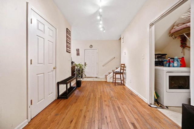 hallway featuring baseboards, stairs, rail lighting, light wood-style floors, and washer / clothes dryer