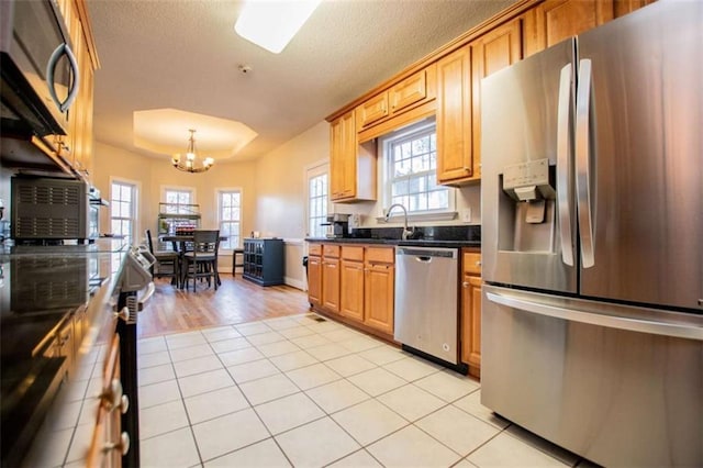 kitchen with dark countertops, appliances with stainless steel finishes, an inviting chandelier, light tile patterned floors, and a raised ceiling