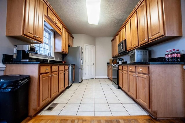 kitchen with light tile patterned floors, visible vents, appliances with stainless steel finishes, a textured ceiling, and brown cabinets