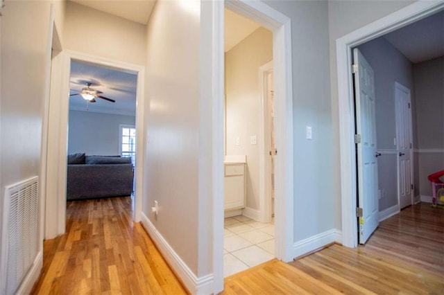 corridor with light wood-style floors, visible vents, and baseboards