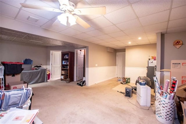 finished basement with carpet flooring, wainscoting, ceiling fan, and a drop ceiling