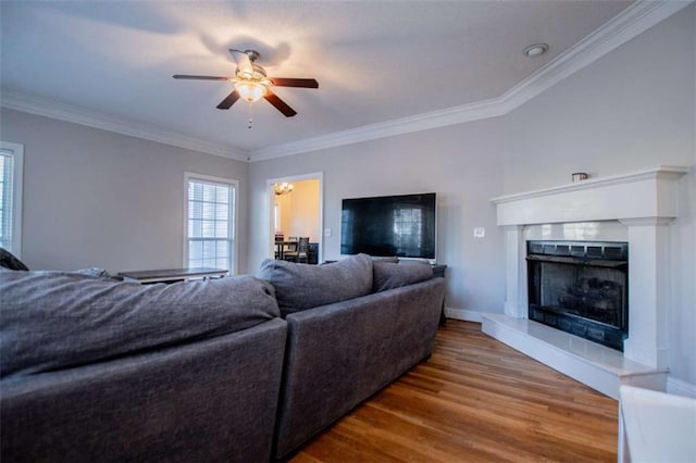 living area featuring a fireplace with raised hearth, crown molding, ceiling fan, and wood finished floors