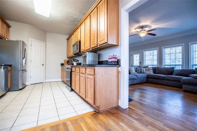 kitchen with dark countertops, appliances with stainless steel finishes, light wood-style floors, a textured ceiling, and a ceiling fan