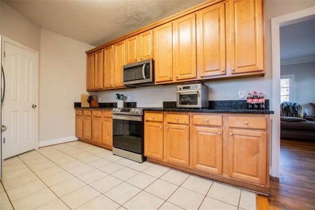 kitchen featuring light tile patterned floors, dark stone counters, a textured ceiling, and appliances with stainless steel finishes