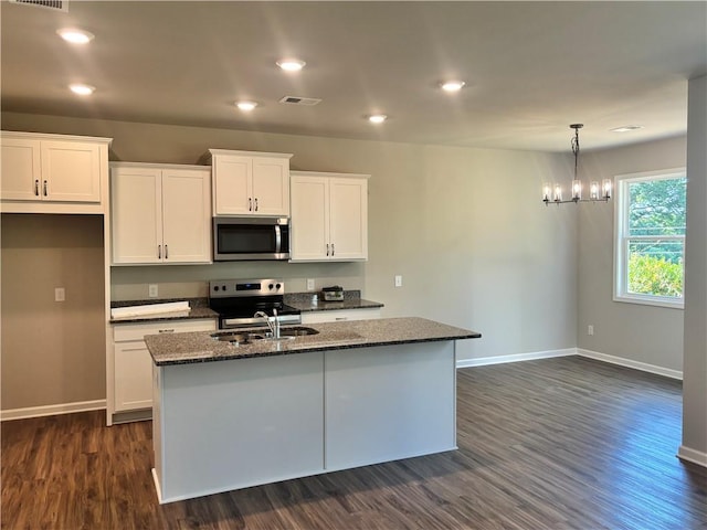 kitchen featuring a center island with sink, white cabinetry, stainless steel appliances, and dark stone counters