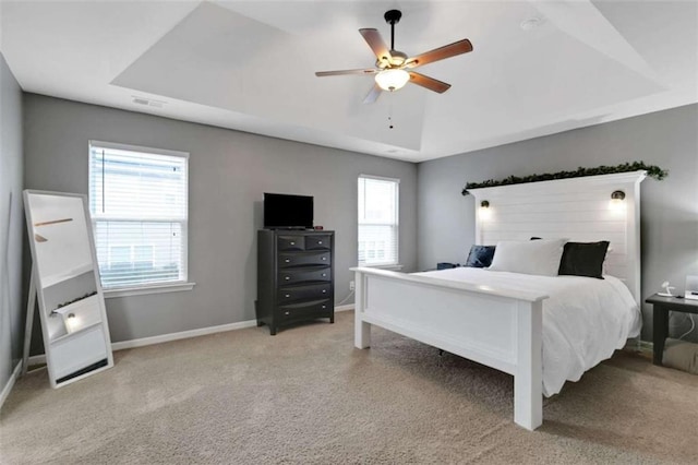 bedroom with a tray ceiling, carpet, a ceiling fan, and baseboards