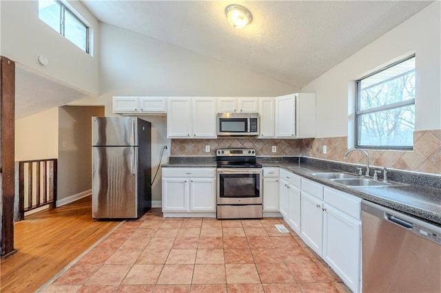 kitchen featuring stainless steel appliances, dark countertops, a sink, and white cabinetry