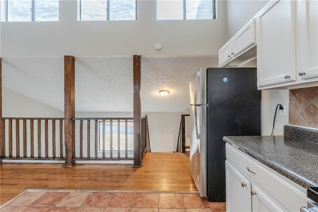 kitchen with dark countertops, backsplash, freestanding refrigerator, white cabinets, and light tile patterned flooring