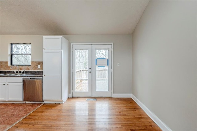 kitchen featuring french doors, light wood finished floors, dark countertops, a sink, and dishwasher