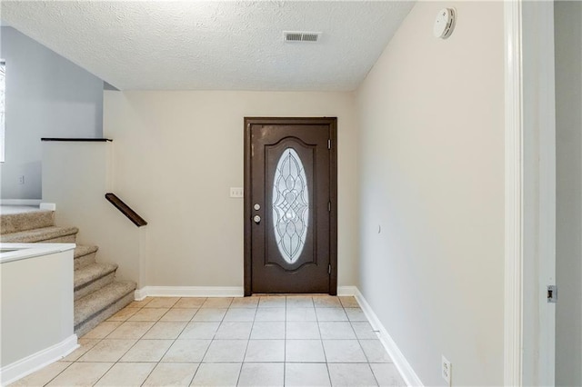 entryway featuring light tile patterned floors, a textured ceiling, visible vents, baseboards, and stairs