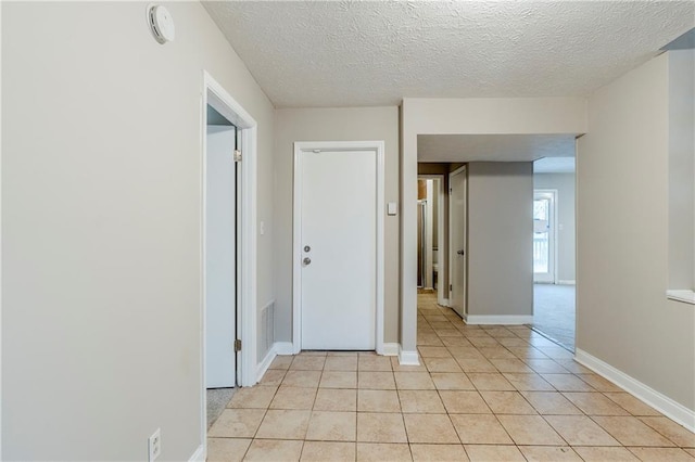 empty room with light tile patterned flooring, a textured ceiling, and baseboards