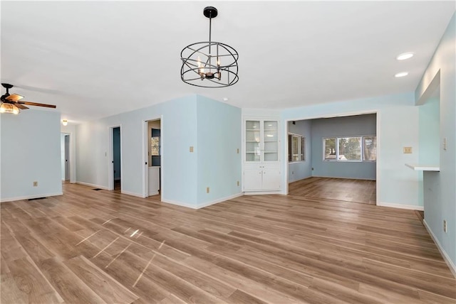 unfurnished living room featuring ceiling fan with notable chandelier and light wood-type flooring