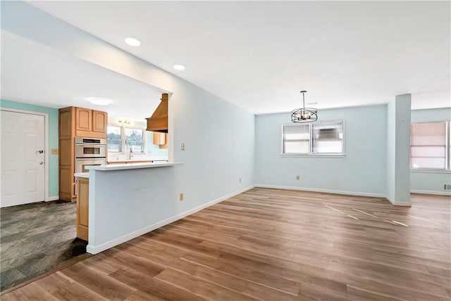 kitchen with a notable chandelier, kitchen peninsula, stainless steel double oven, and dark wood-type flooring