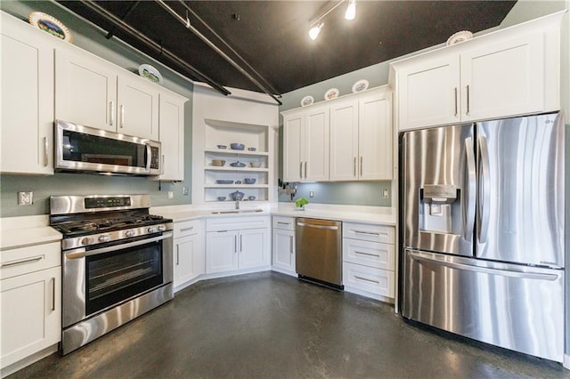 kitchen with light countertops, appliances with stainless steel finishes, white cabinets, a sink, and concrete floors