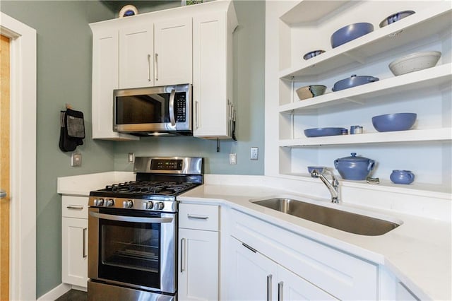 kitchen featuring stainless steel appliances, a sink, white cabinetry, light countertops, and open shelves