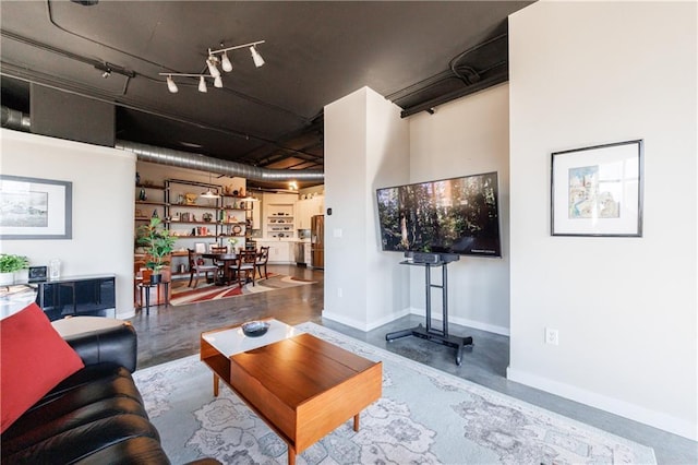 living area featuring rail lighting, finished concrete floors, and baseboards