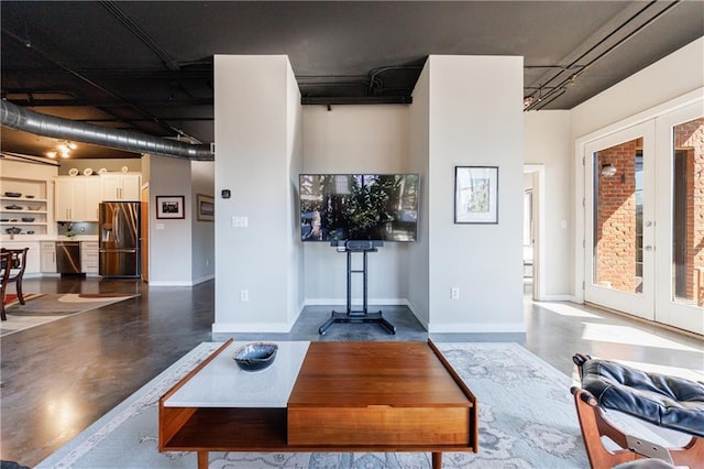 living area with finished concrete flooring, baseboards, and french doors