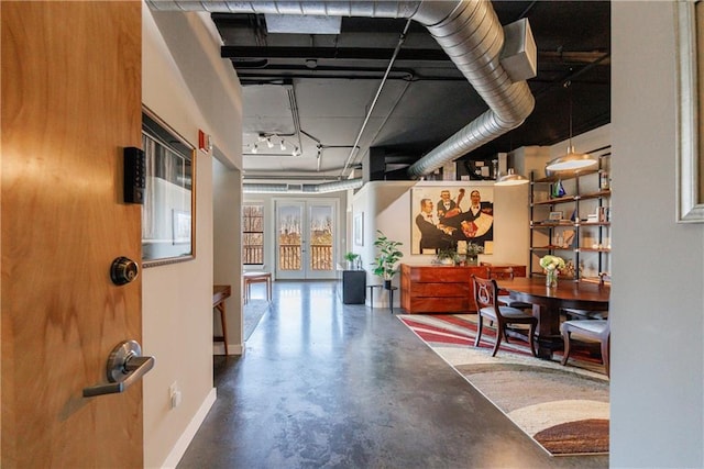 corridor featuring french doors, finished concrete flooring, and baseboards