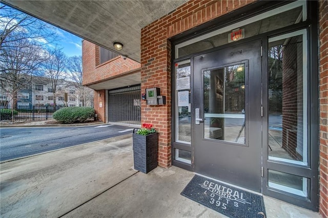 view of exterior entry featuring brick siding and fence