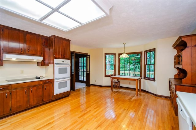 kitchen with pendant lighting, black electric stovetop, white double oven, and light wood-type flooring