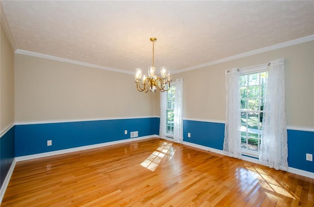 spare room with an inviting chandelier, wood-type flooring, and ornamental molding