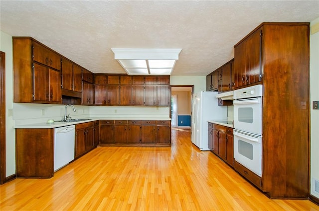 kitchen with sink, white appliances, light hardwood / wood-style flooring, and a textured ceiling