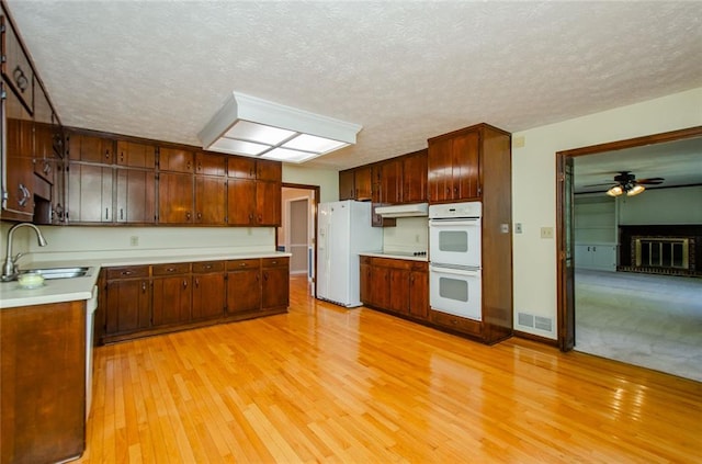 kitchen with sink, white appliances, ceiling fan, a brick fireplace, and light wood-type flooring