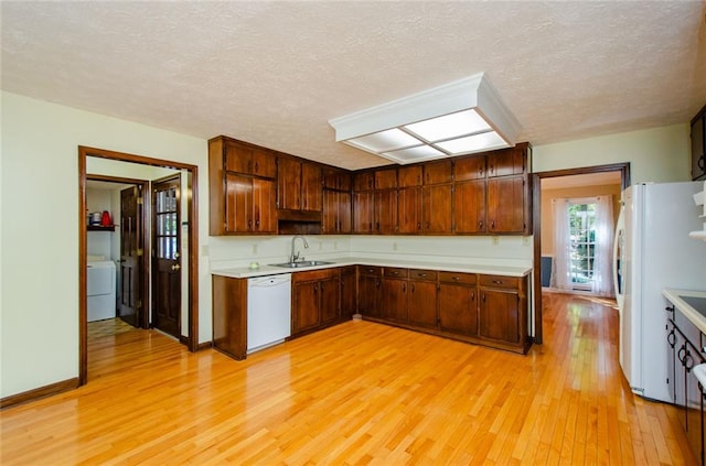 kitchen featuring sink, white appliances, light hardwood / wood-style floors, a textured ceiling, and washer / clothes dryer