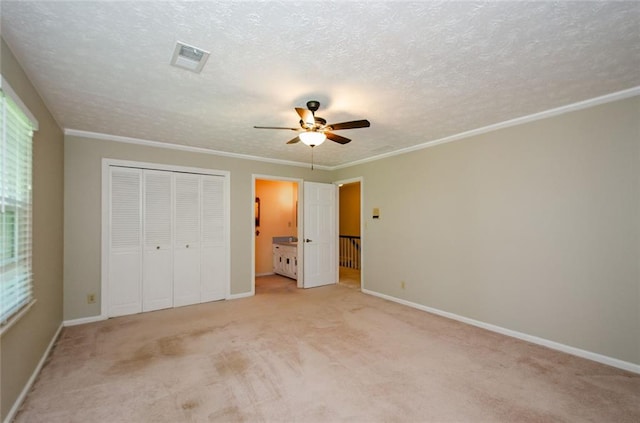 unfurnished bedroom with light colored carpet, ornamental molding, a closet, and a textured ceiling