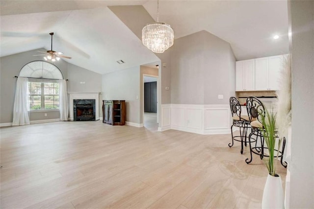 living room featuring a premium fireplace, light hardwood / wood-style flooring, ceiling fan with notable chandelier, and vaulted ceiling