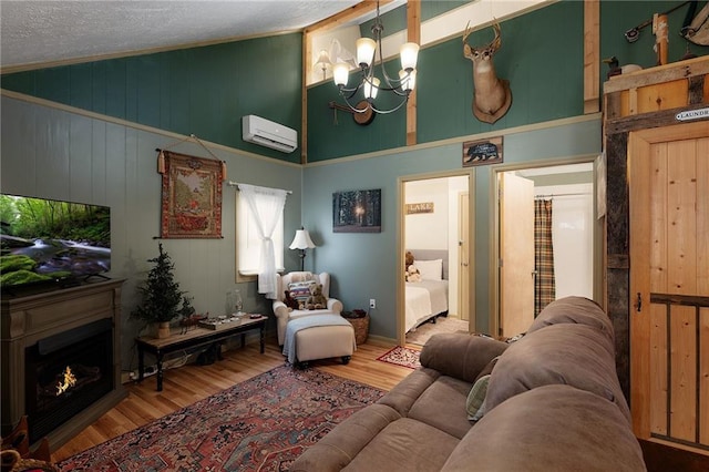 living room with wood finished floors, high vaulted ceiling, a warm lit fireplace, a wall mounted air conditioner, and a notable chandelier