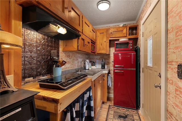 kitchen with a sink, under cabinet range hood, a textured ceiling, black electric stovetop, and brown cabinets