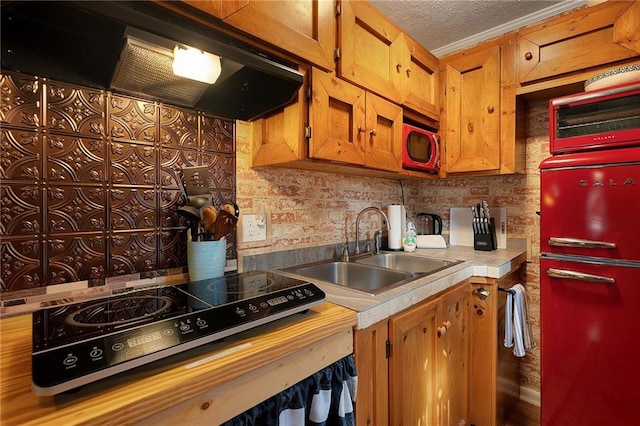 kitchen with extractor fan, tile counters, brown cabinets, a textured ceiling, and a sink