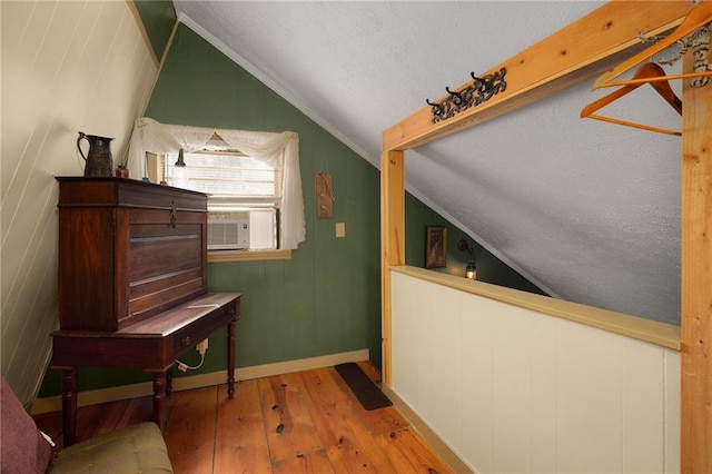 corridor featuring hardwood / wood-style floors, cooling unit, baseboards, lofted ceiling, and a textured ceiling