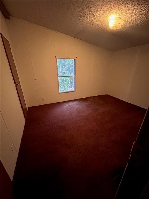 unfurnished room featuring dark carpet, a textured ceiling, and vaulted ceiling