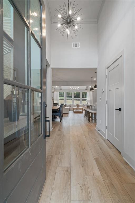 hall featuring crown molding, wood finished floors, visible vents, and an inviting chandelier