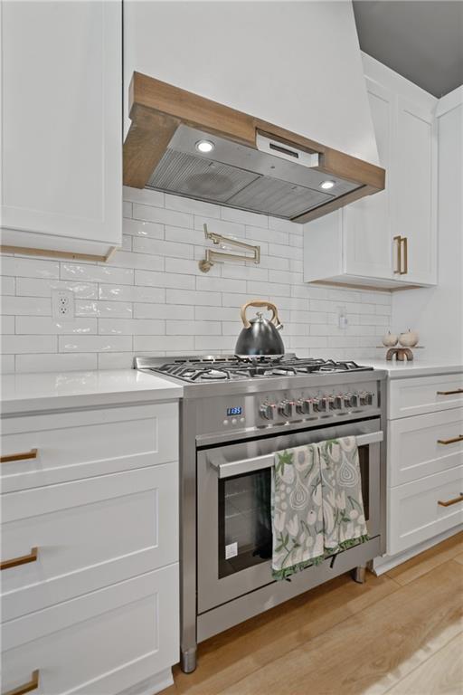 kitchen featuring wall chimney range hood, white cabinetry, high end range, and light countertops