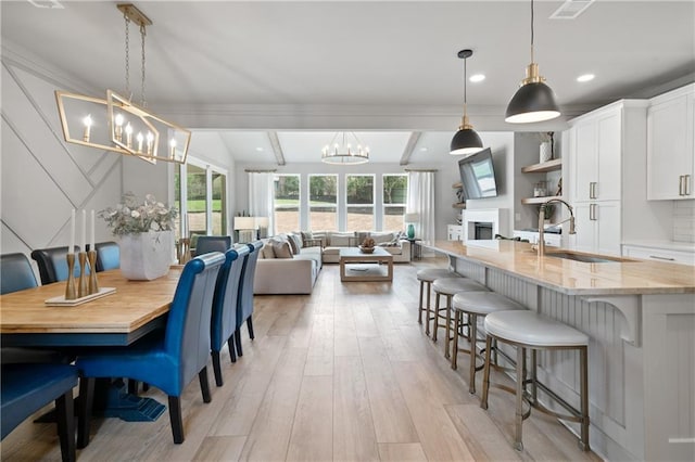 dining area with a chandelier, a fireplace, visible vents, light wood finished floors, and beamed ceiling