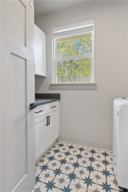 clothes washing area with light floors, cabinet space, and baseboards