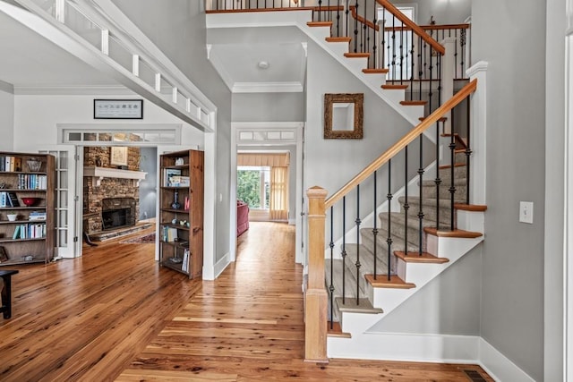 foyer with crown molding, a stone fireplace, and hardwood / wood-style floors