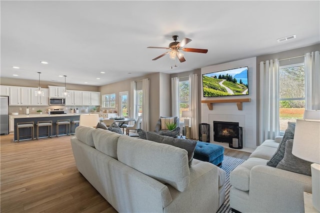 living room with a large fireplace, light wood-type flooring, and ceiling fan