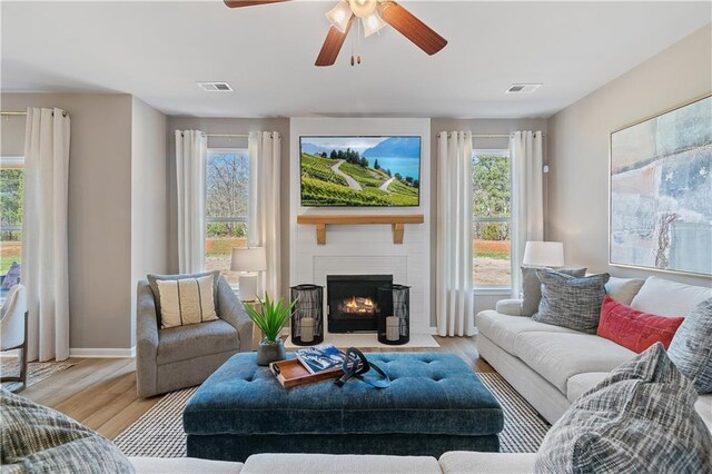 living room featuring ceiling fan, light hardwood / wood-style flooring, and a fireplace