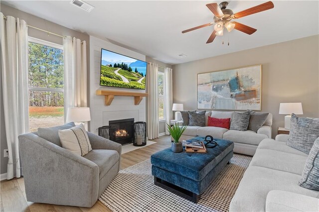 living room featuring a fireplace, ceiling fan, light wood-type flooring, and a wealth of natural light